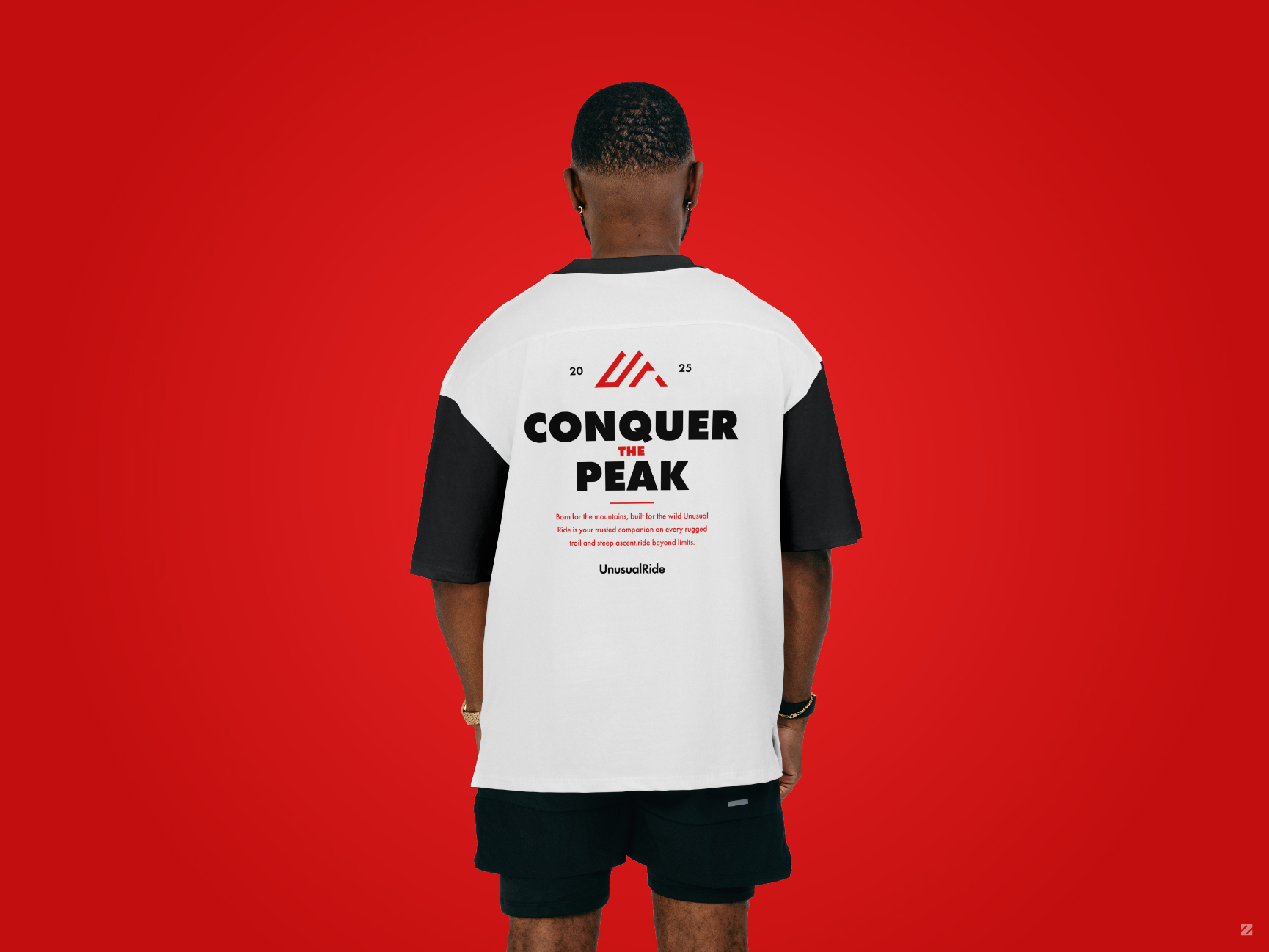 Model wearing white and black oversized UnusualRide t-shirt with "Conquer the Peak" back print design on red background